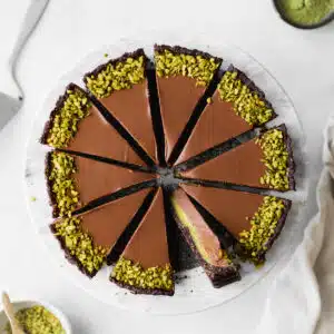 chocolate tart with pistachios cut into slices on a marble platter.
