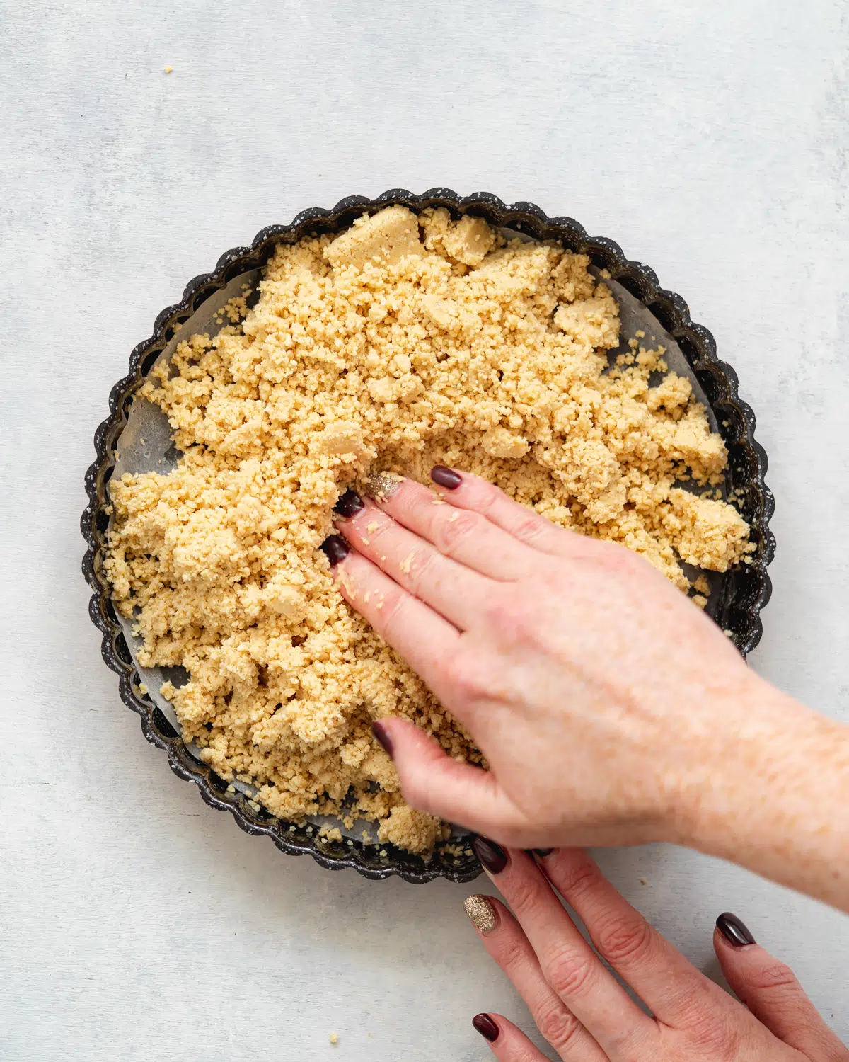 hand pressing pastry crumbs into the base of a tart tin.