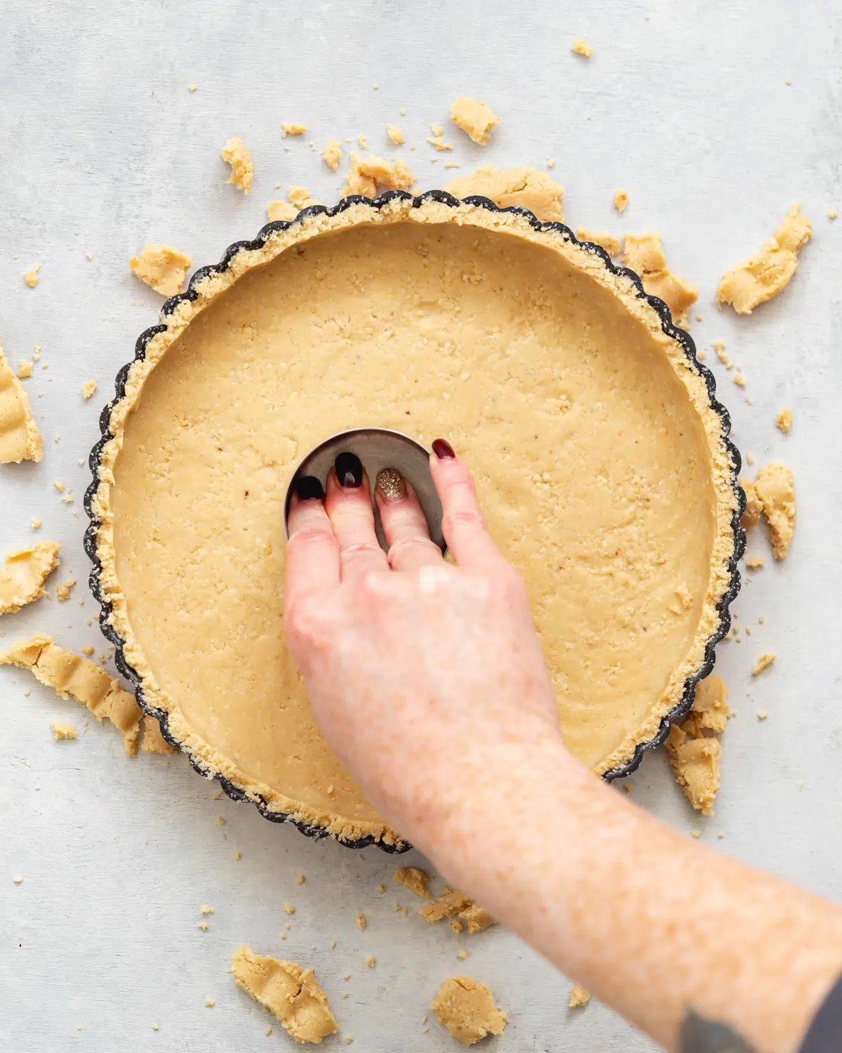 hand pressing down pastry into the base of a tart shell using a cup measure.