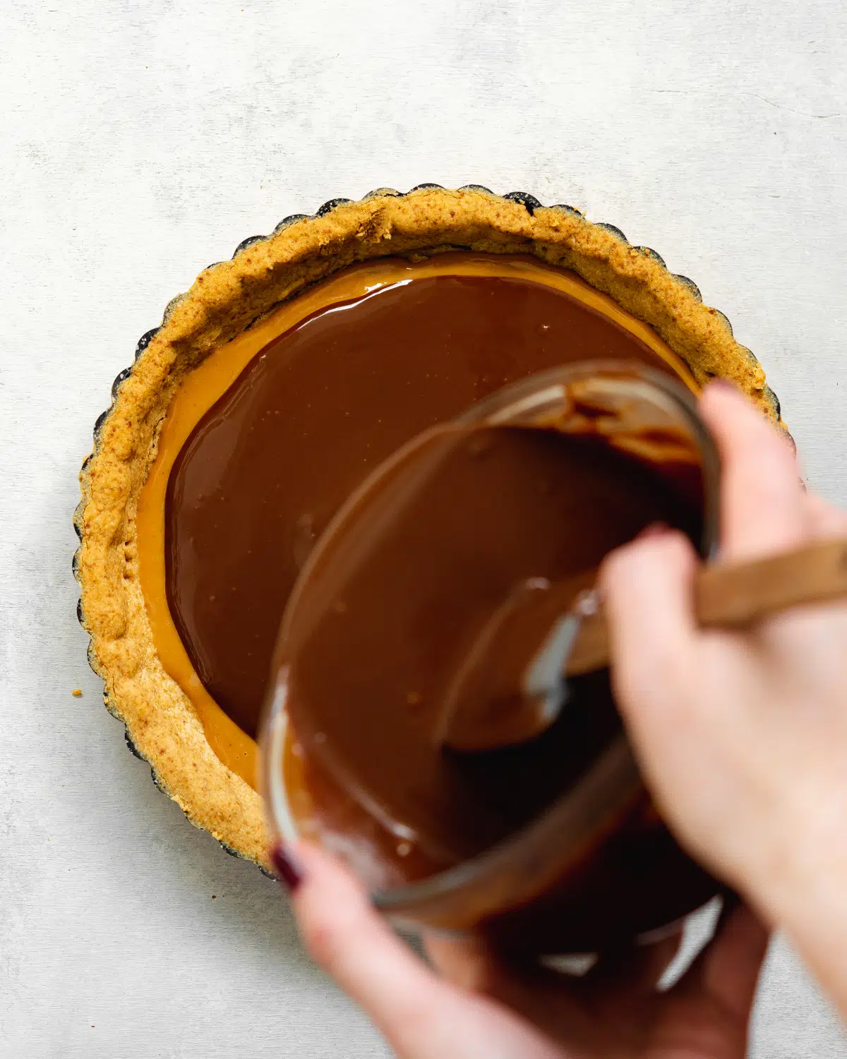 pouring chocolate ganache into a pastry tart tin.