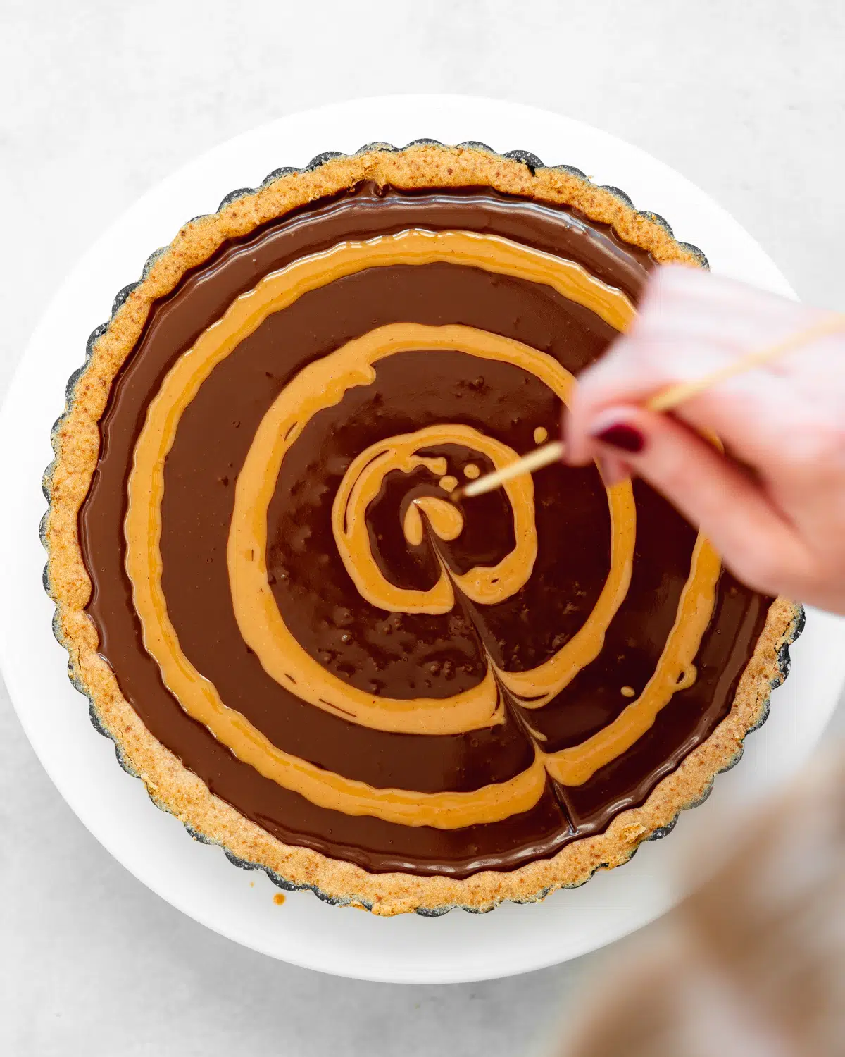creating a swirl pattern with peanut butter on top of a chocolate tart using a skewer.