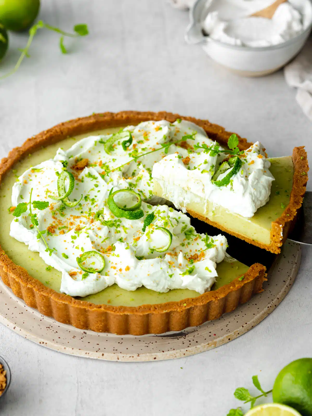 vegan key lime pie topped with dairy free whipped cream and fresh lime zest on a ceramic plate.