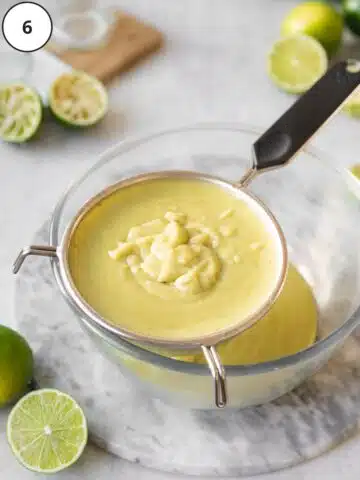 lime curd filling for dairy free lime pie being passed through a fine-mesh sieve and collected in a glass mixing bowl.
