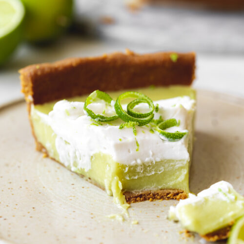a slice of vegan key lime pie on a ceramic plate. There is a spoonful taken from it, showing the creamy consistency.