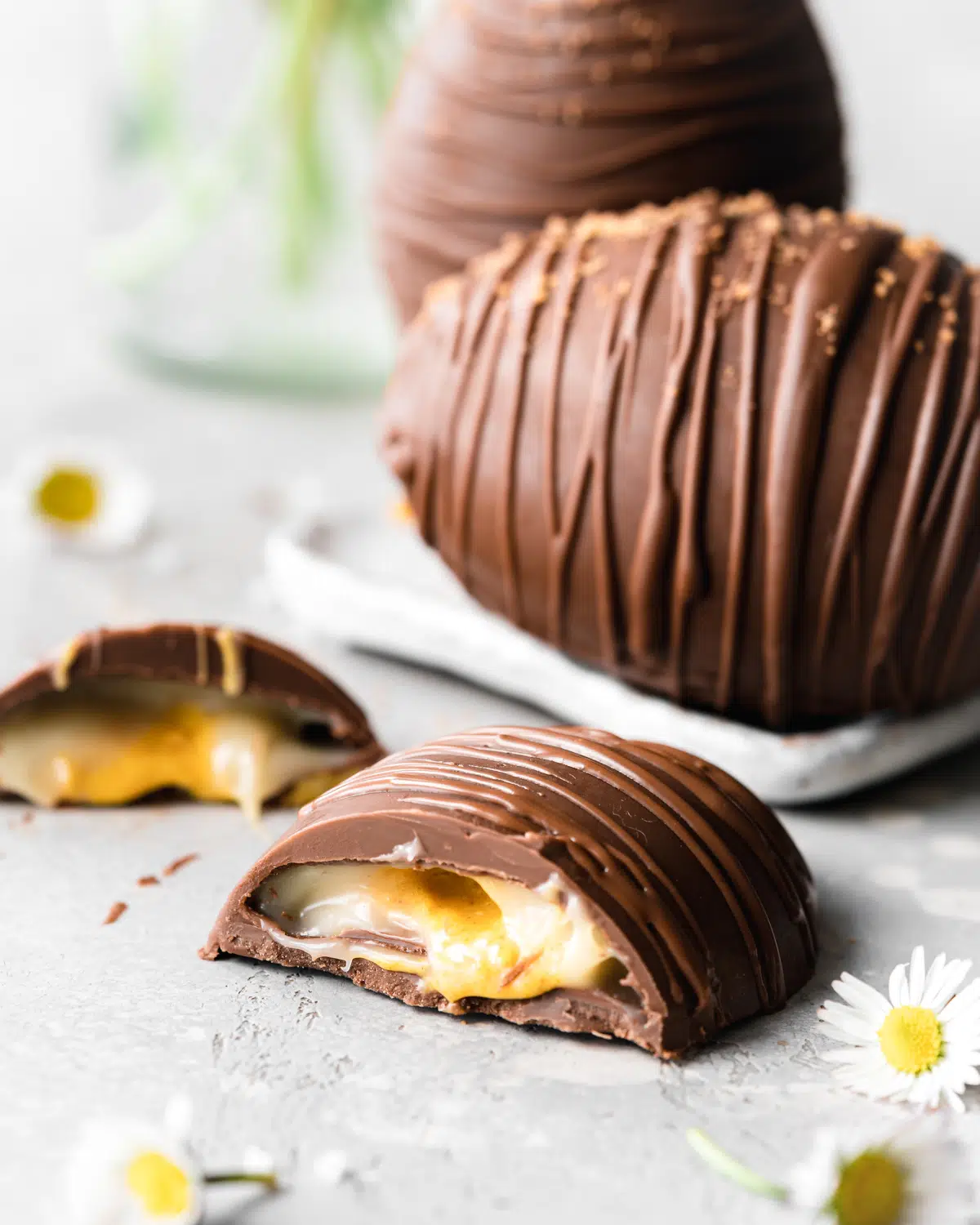 giant creme egg cut in half with daisies in the foreground.