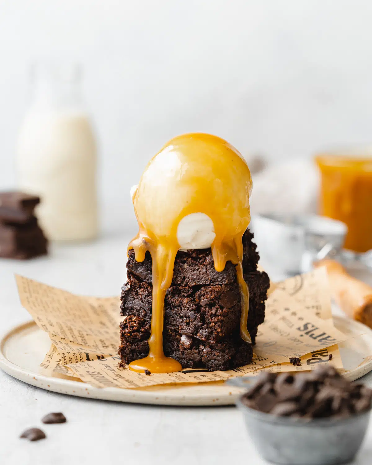 stack of fudgy gooey vegan brownies on brown paper with ice cream and caramel sauce on top.