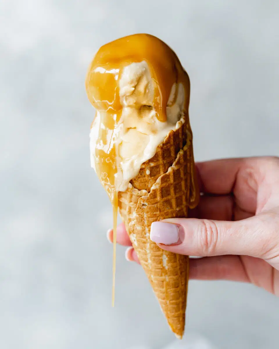 hand holding up ice cream cone with caramel sauce dripping from it.