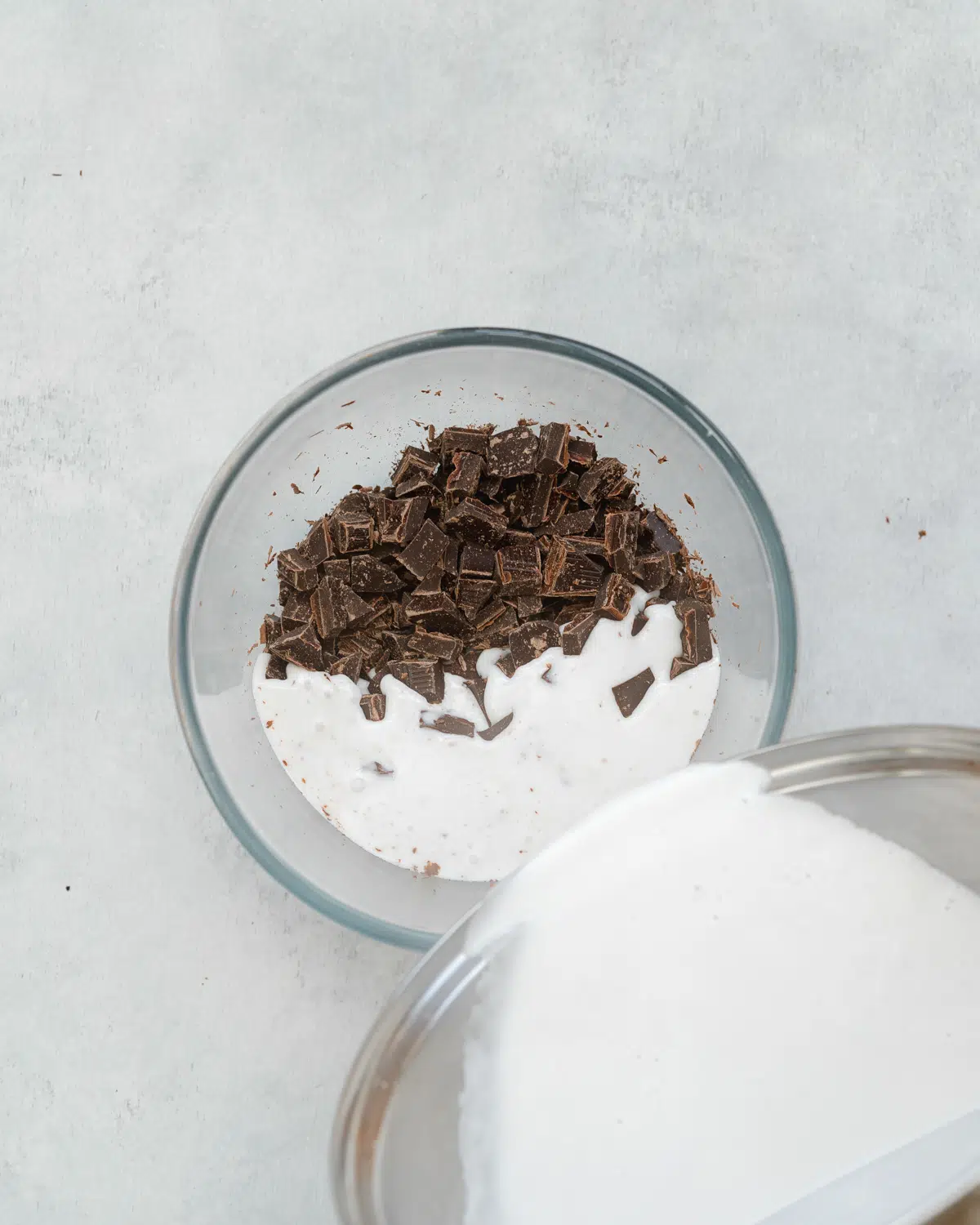 pouring warm coconut milk into a bowl of chopped chocolate.
