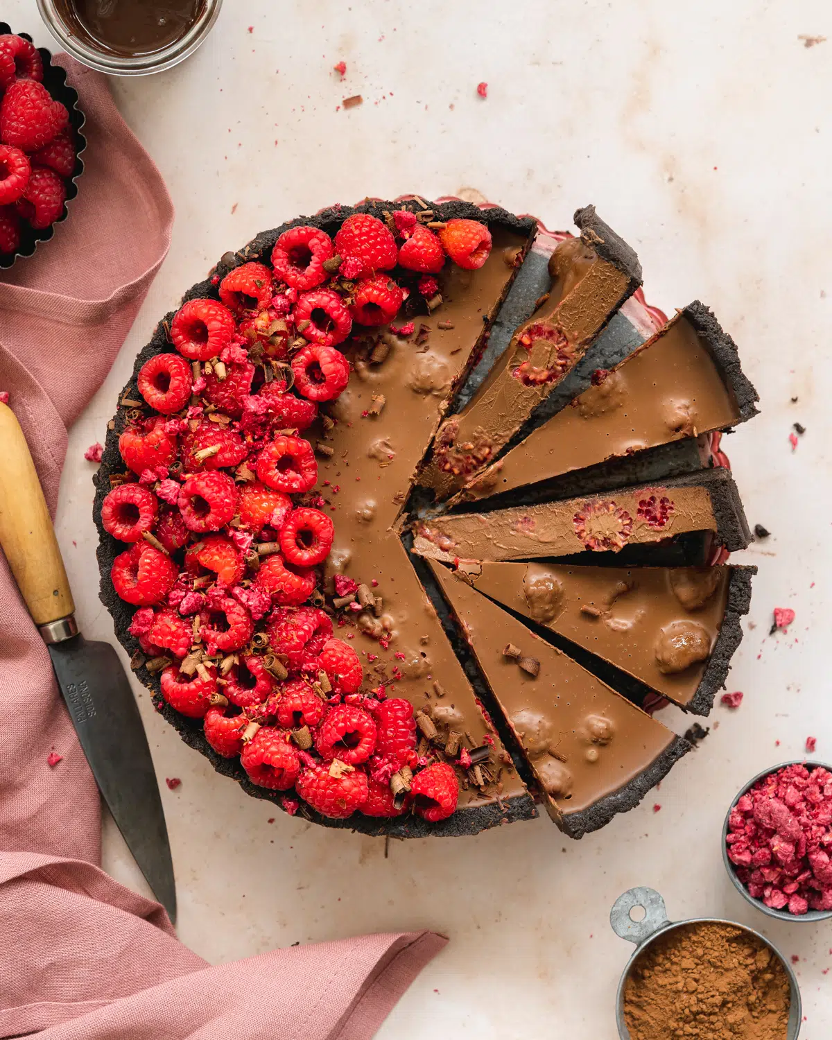 flat lay of chocolate tart with fresh raspberries and pink linens.