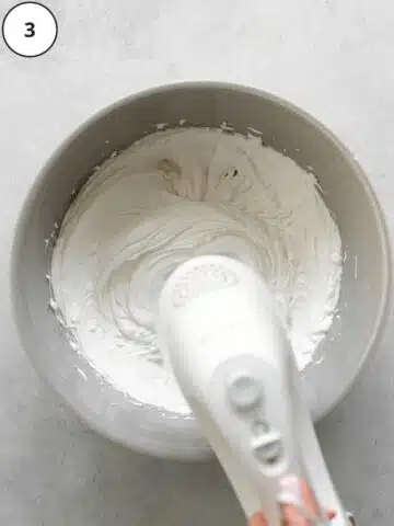 whisking coconut whipping cream in a large mixing bowl with an electric whisk.