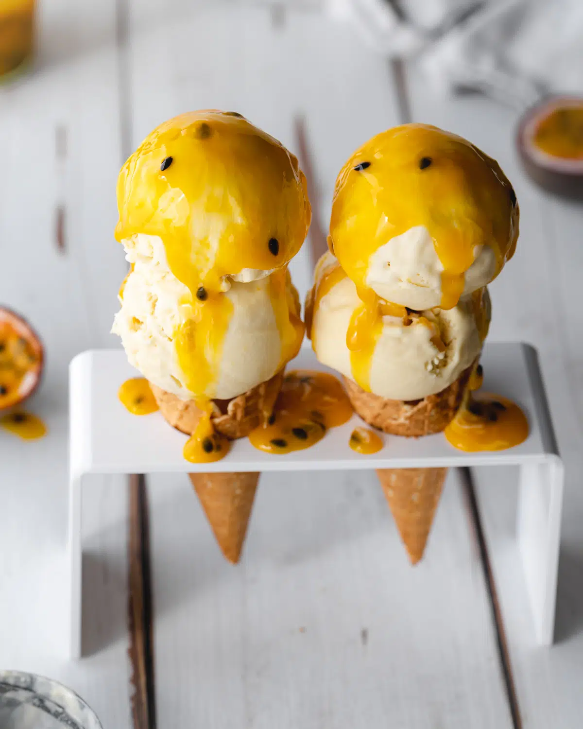 2 passion fruit ice cream cones with passionfruit coulis on a wooden white surface.