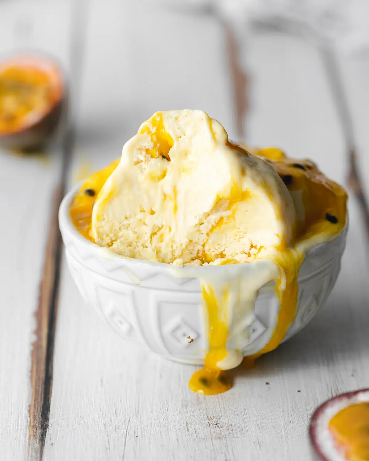 passionfruit ice cream in a small white bowl with passionfruit coulis poured over the top