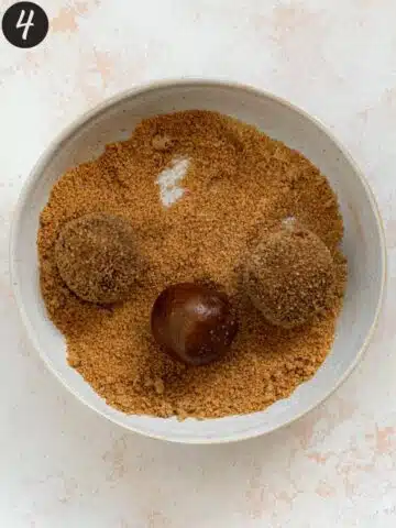 molasses cookie dough balls in a bowl of sugar and cinnamon.