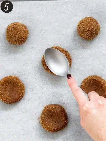 pressing down molasses cookies with the back of a spoon.
