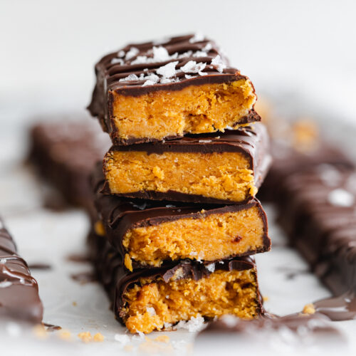 stack of homemade butterfinger chocolate bars with jar of peanut butter in the background.