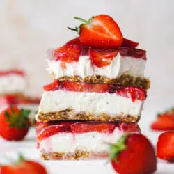 stack of vegan strawberry cheesecake bars with fresh strawberries on top.