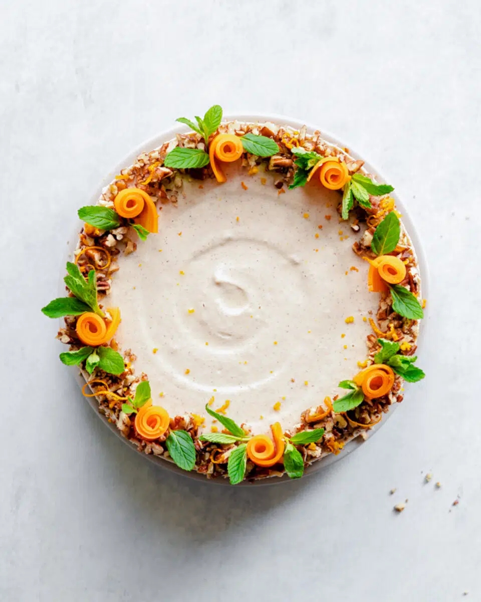 no bake carrot cake cheesecake with mint leaves and candied carrots on a grey concrete surface.