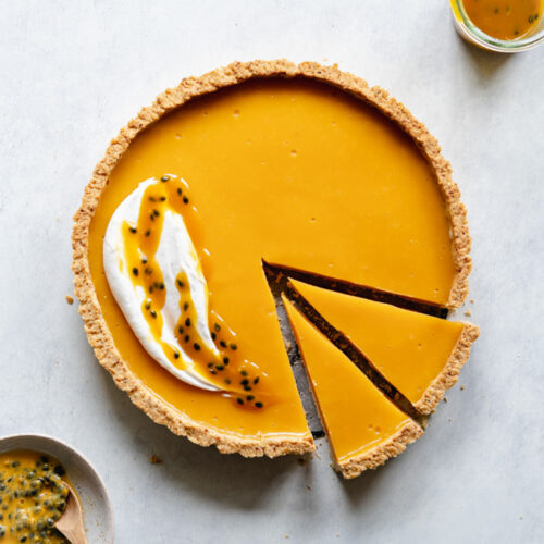 flatlay of passion fruit tart with cream on a grey concrete surface.