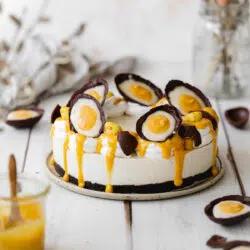 cheesecake with decorated with homemade creme eggs on a white wooden surface.