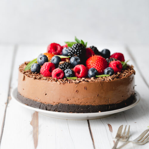 chocolate mousse cake with fresh berries and mint leaves on top on a white wooden surface.
