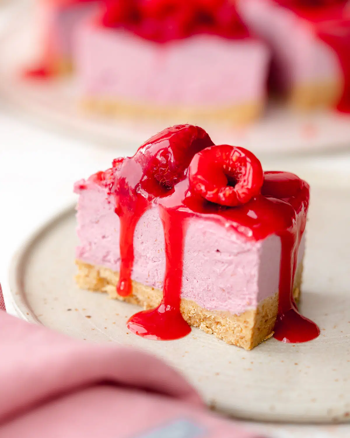 slice of pink cheesecake with raspberry glaze and fresh berries on top.