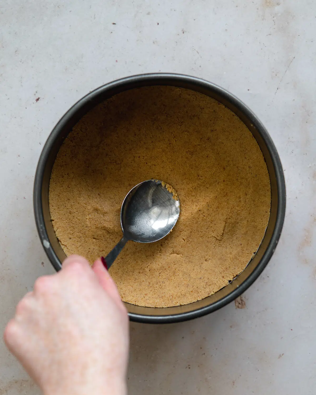 pressing cookie base into a cake pan using a spoon.