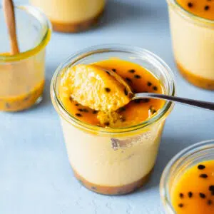jars of mango mousse with spoon on blue surface.
