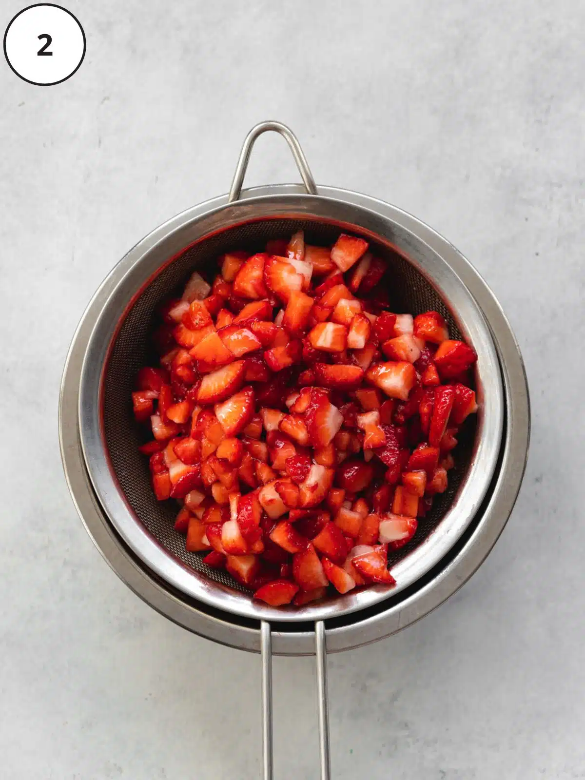 dced strawberries straining over a fine-mesh sieve with a saucepan collecting the juices.