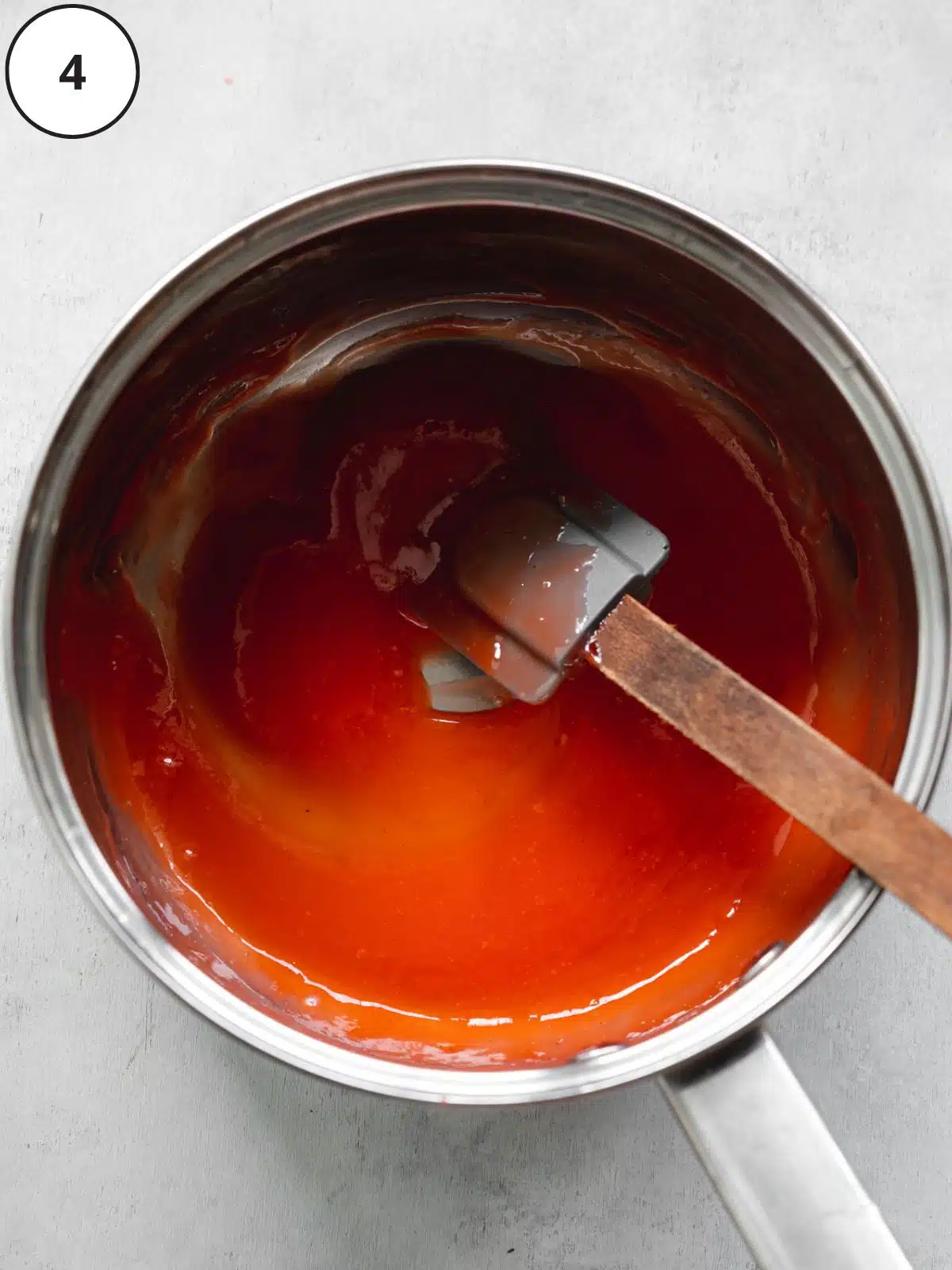 reduced strawberry coulis in a saucepan with a spatula showing the thick consistency.