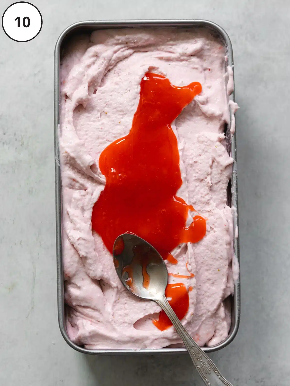 a spoon swirling strawberry coulis on top of strawberry ice cream.