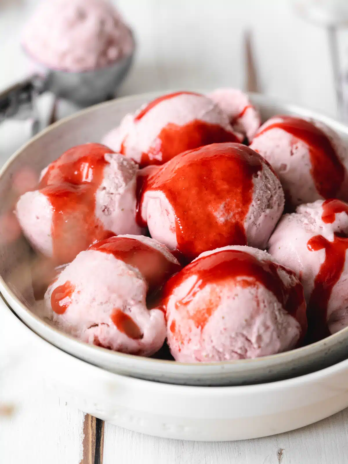 a bowl filled with scoops of homemade vegan ice cream drenched in strawberry coulis.