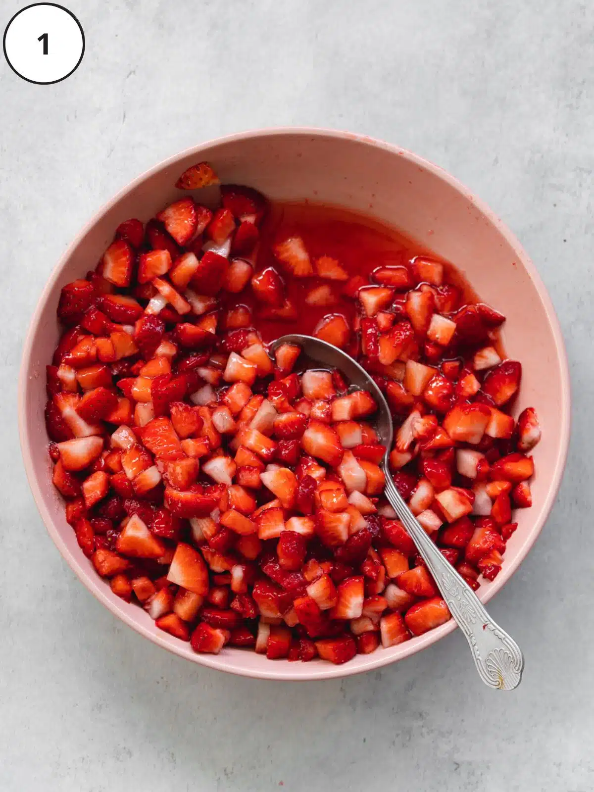 strawberry chunks macerating in in a large bowl with sugar, showing the juices being released from the berries.