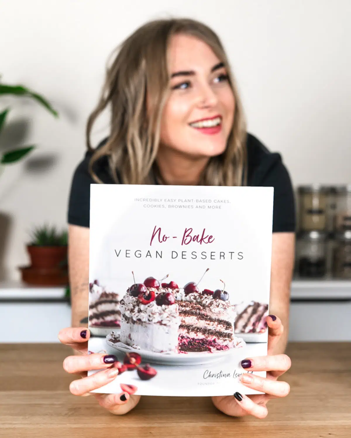 vegan desserts cookbook author holding up a book with a picture of a vegan cake on it.