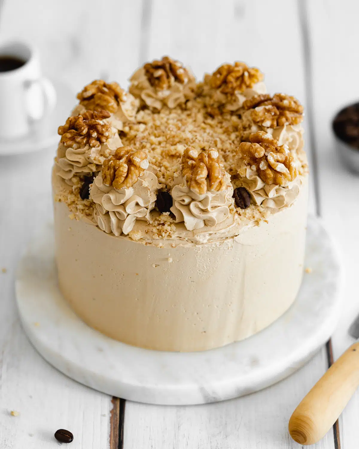 vegan coffee and walnut layer cake on white wooden backdrop.