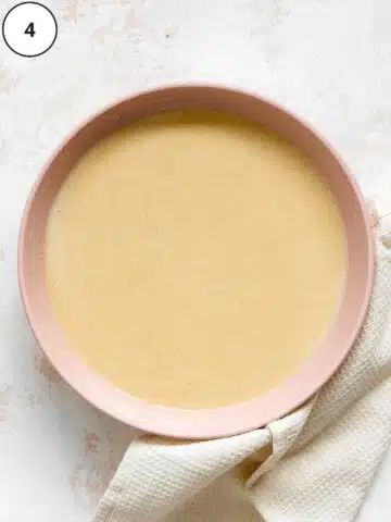 melted dairy-free white chocolate in a pink bowl with a gray towel around it.