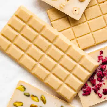 bars of homemade vegan white chocolate laid flat on top of one another, some have nuts and freeze-dried berries.