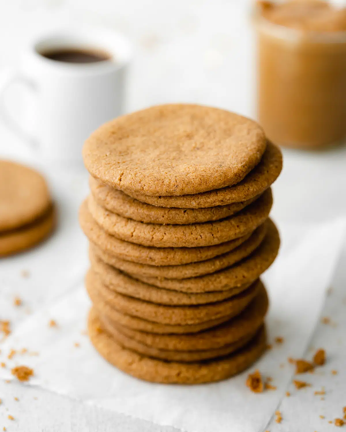 stack of vegan biscoff cookies with coffee and a jar of cookie butter in the background.