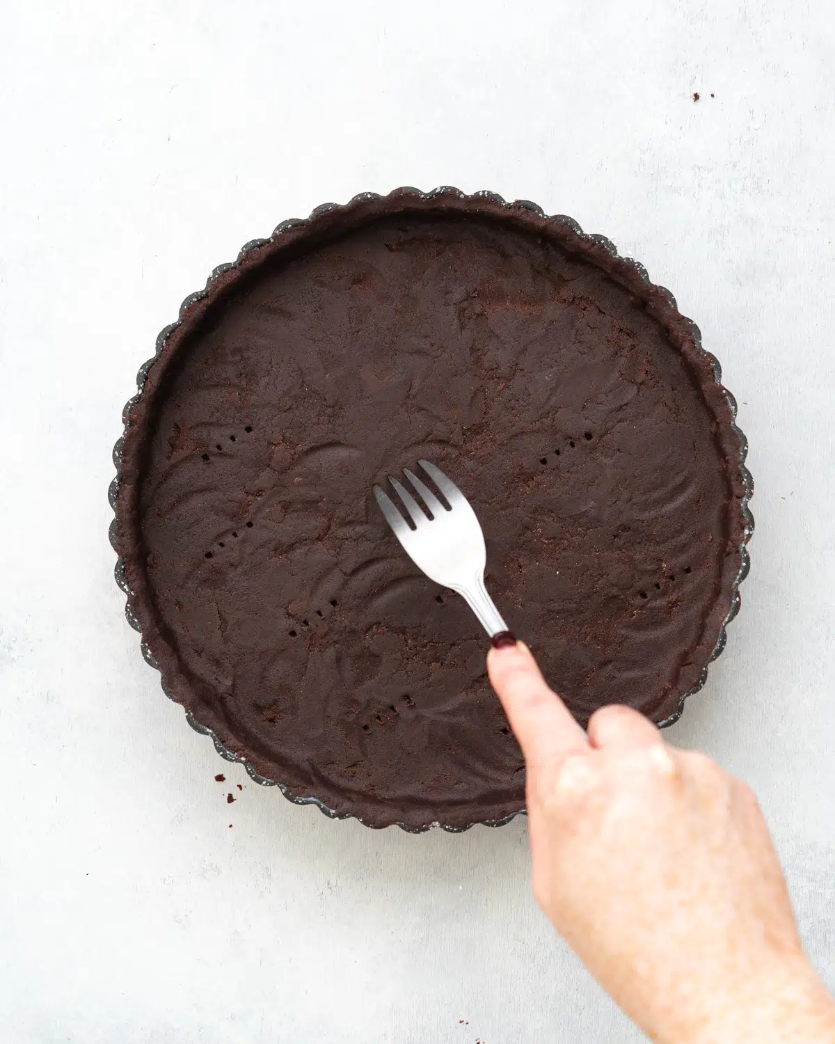 chocolate shortcrust pastry in a tart tin with hand using a fork to prick air holes in the base.