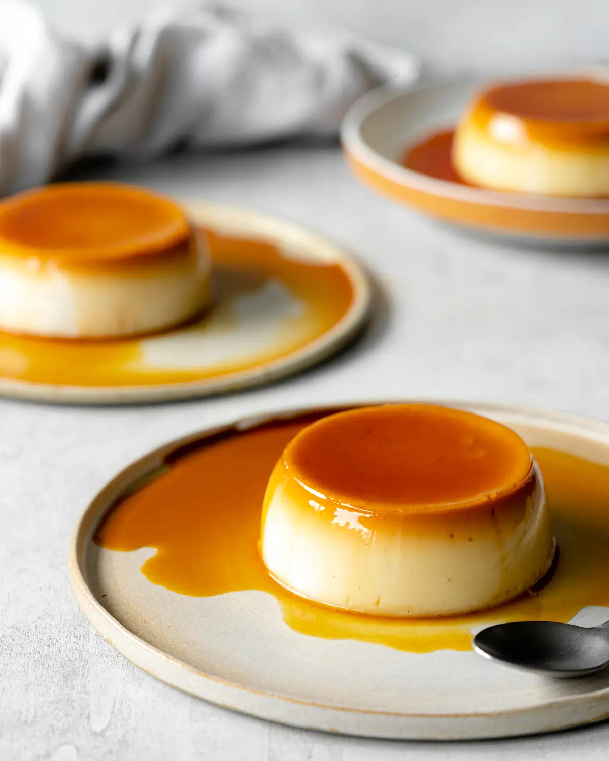 three flans on plates covered in caramel sauce.
