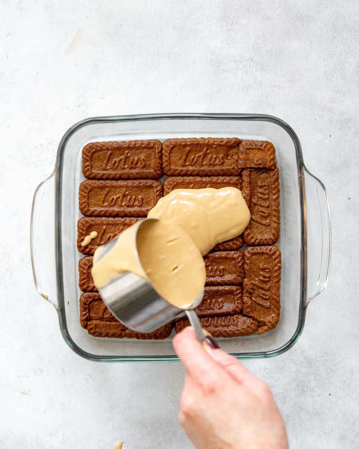 pouring biscoff mascarpone on top of soaked speculoos cookies.