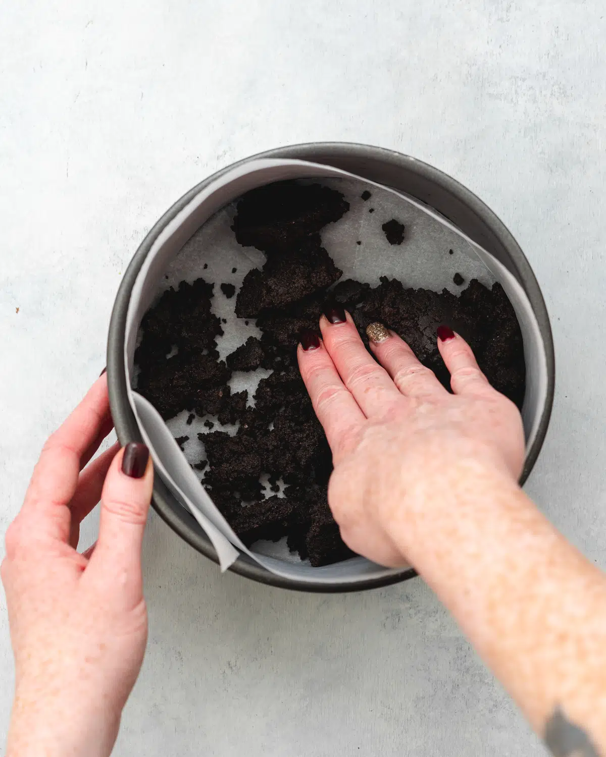 hands pressing cookie crust into the base of a cake tin.