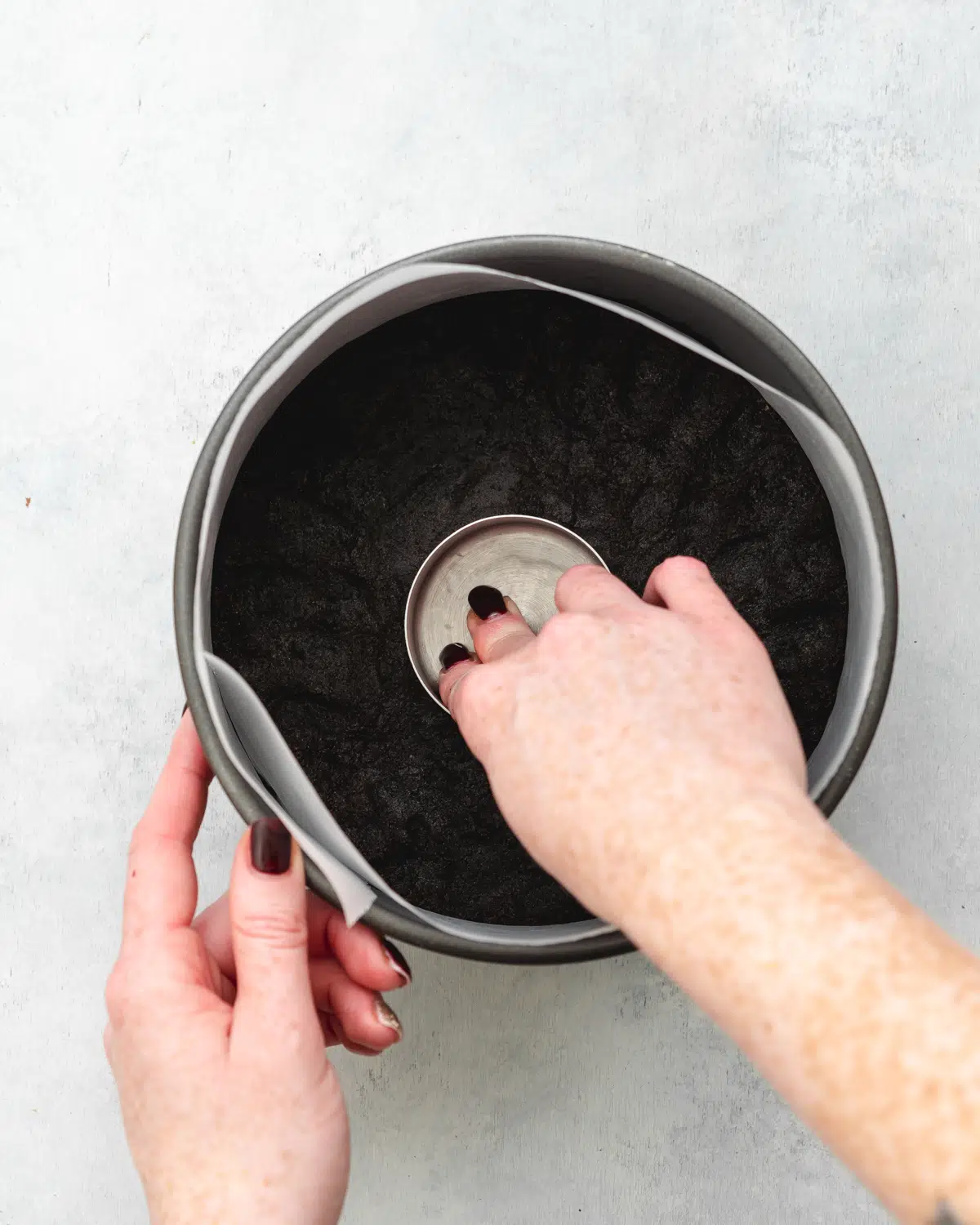 hand using cup measure to press cookie crust into the base of a cake tin.