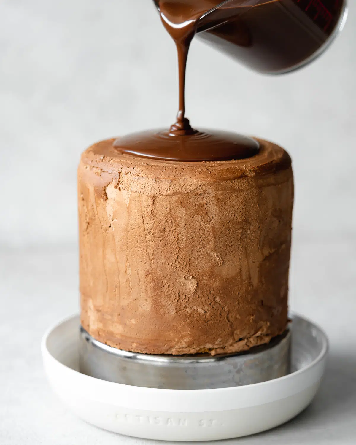 pouring chocolate glaze over chocolate frosted hazelnut cake.