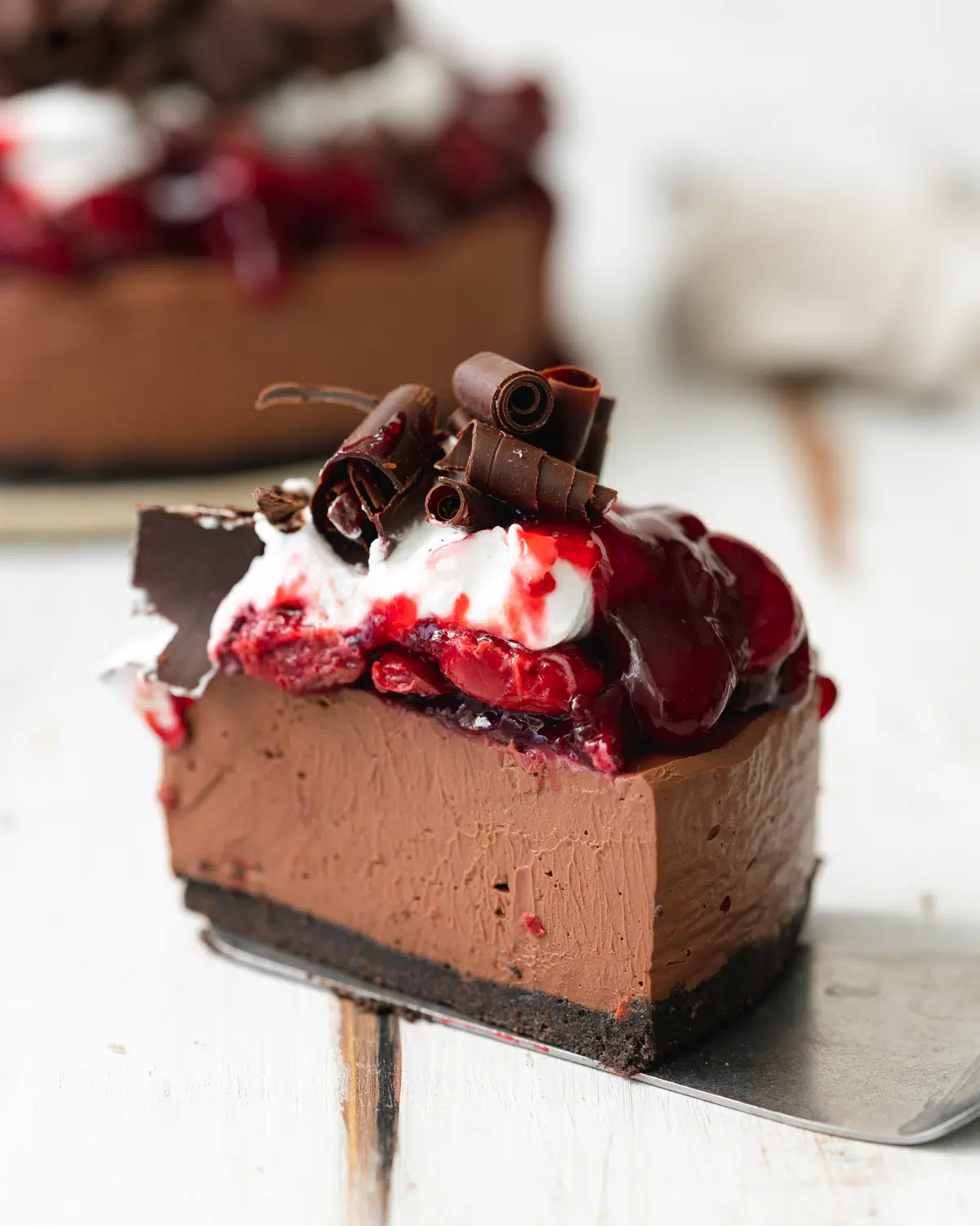 slice of chocolate cheesecake with cherries, cream and chocolate shavings on top.