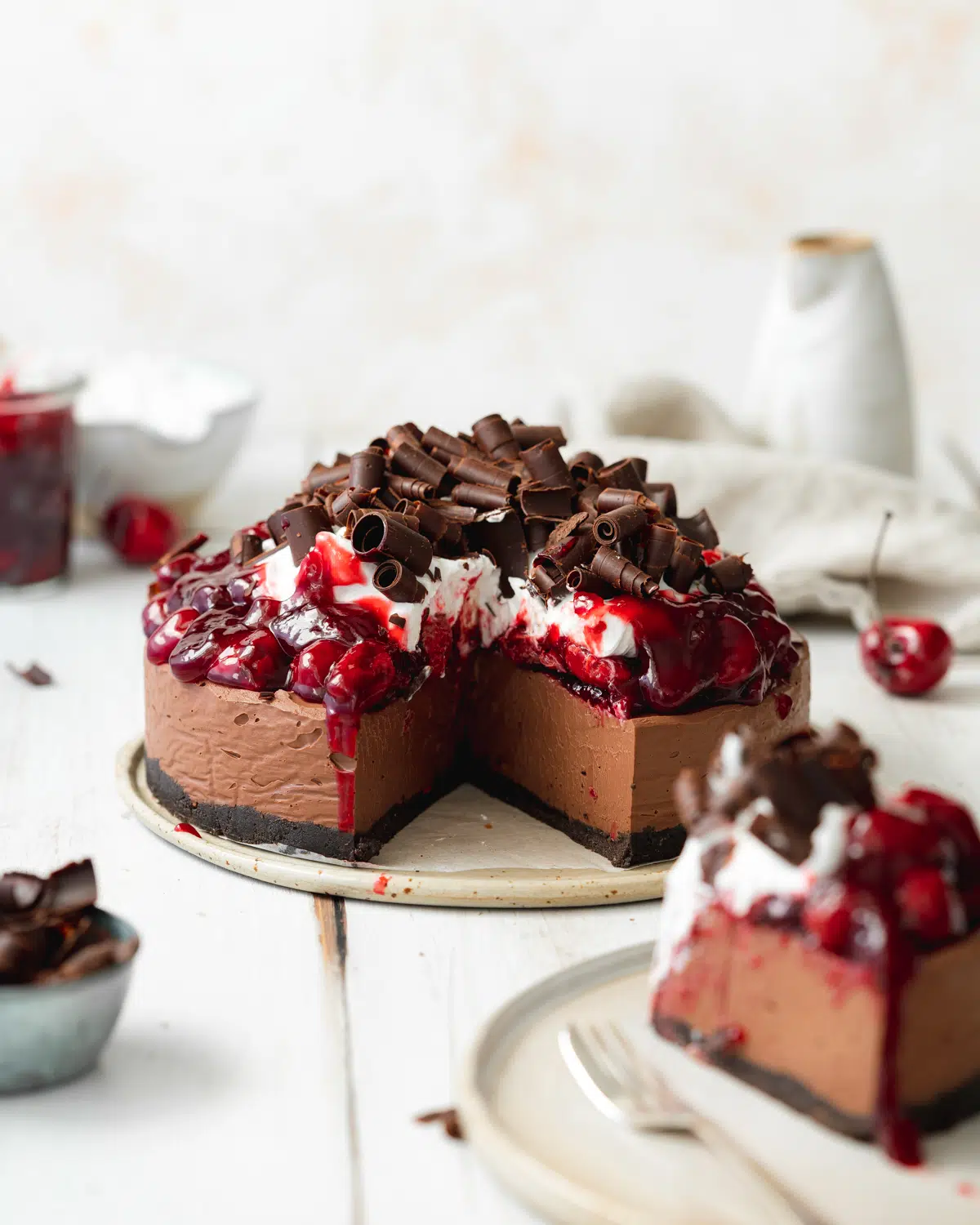 chocolate cherry cheesecake on a white wooden surface with chocolate curls on top.