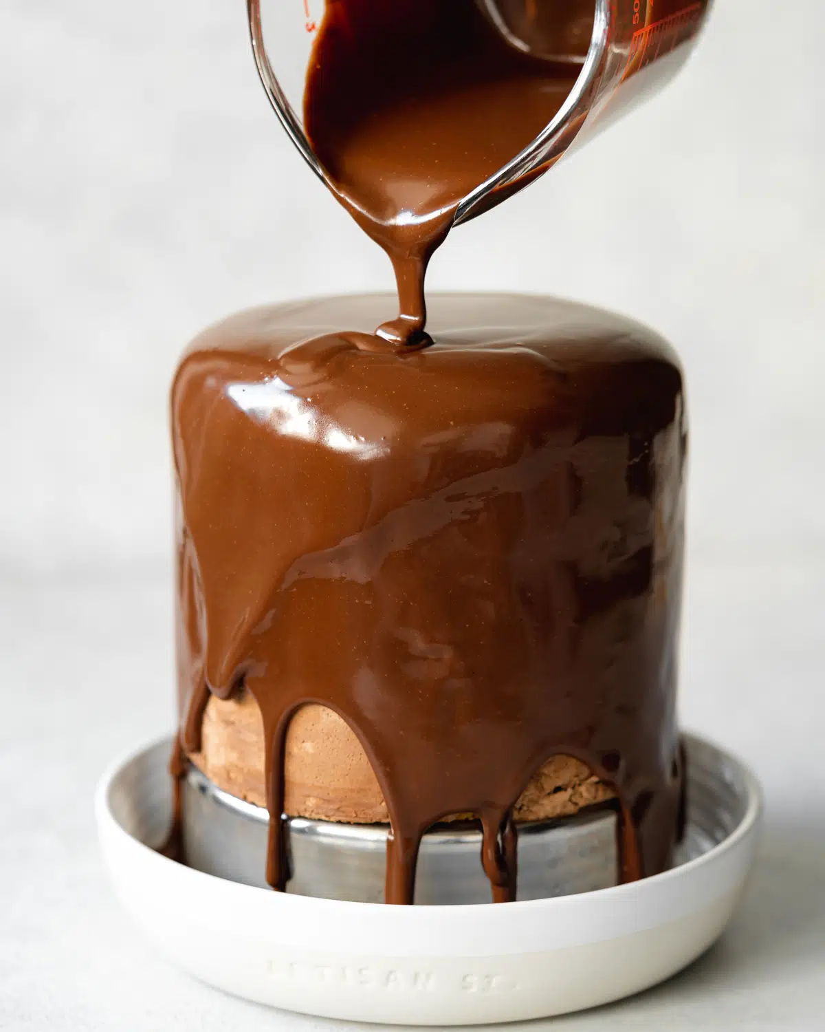 pouring chocolate glaze over chocolate frosted hazelnut cake.