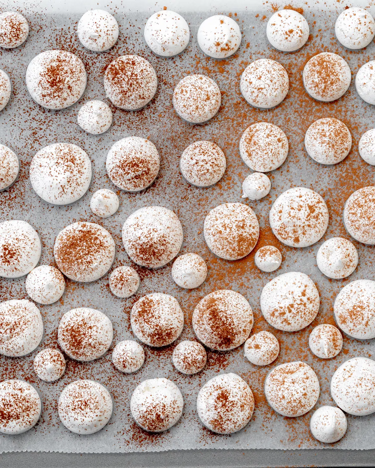 aquafaba meringue cookies dusted with cocoa powder on a baking sheet.