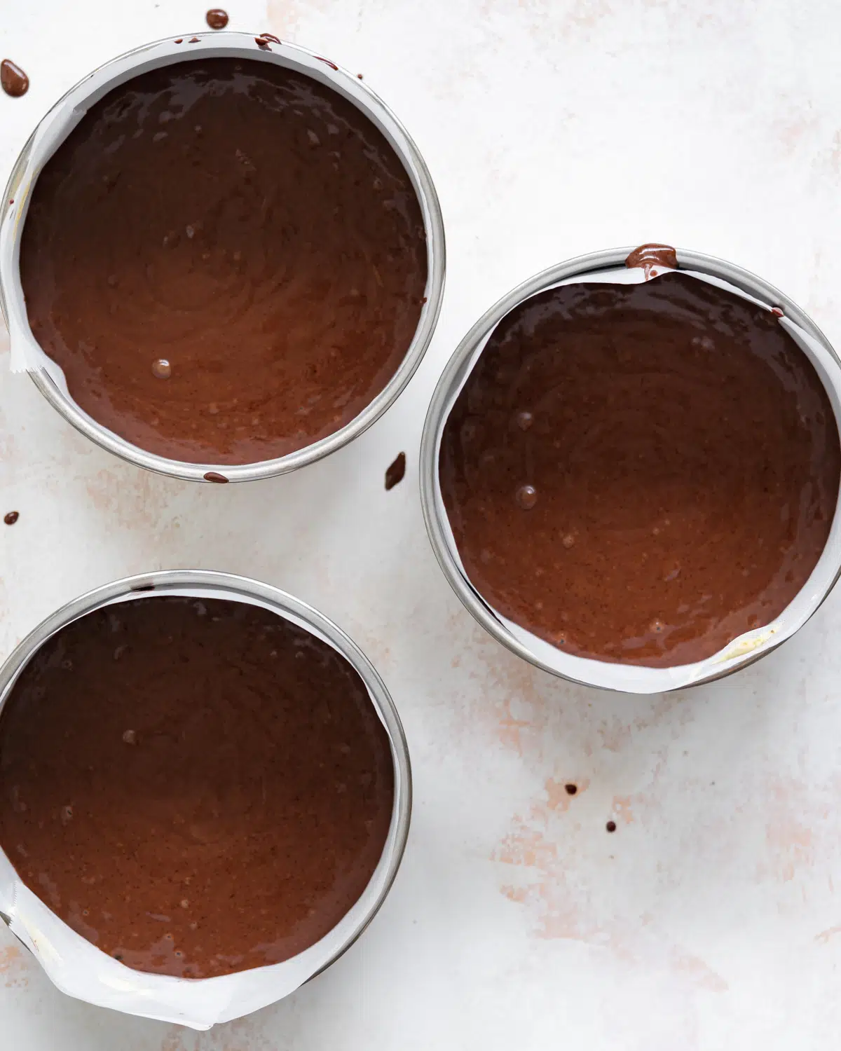 3 cake tins filled with chocolate cake batter,