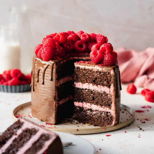 vegan raspberry chocolate layer cake with ganache drip and fresh raspberries on top.