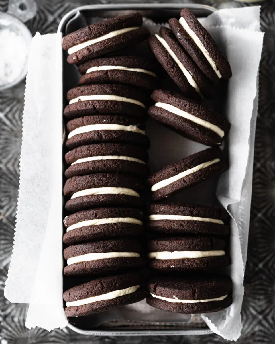 homemade vegan oreos in a tin with parchment paper.